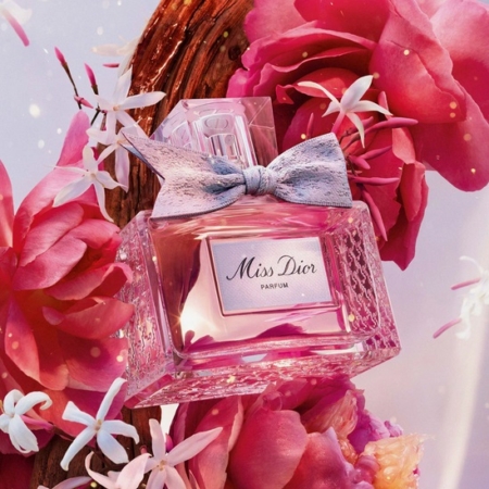 Dior Miss Dior Parfum pour femme, dans un flacon en verre texturé avec un nœud en tissu, se trouve parmi des fleurs et des pétales d'un rose éclatant. Un éclairage doux et chaleureux renforce l'ambiance romantique et élégante. Dakar