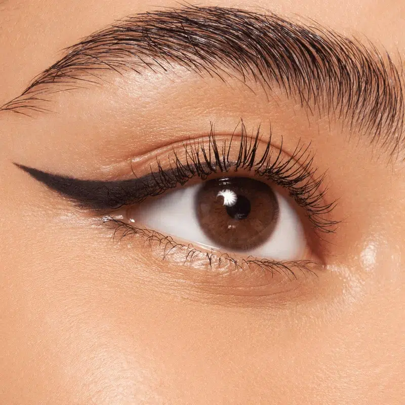 Gros plan sur un œil brun aux longs cils et à l'eyeliner noir parfaitement appliqué, mettant en valeur des sourcils bien dessinés et une peau lisse et naturelle. Dakar