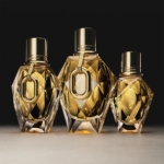 Trois flacons à facettes de l'Eau de Parfum pour Femme Rabanne Million Gold For Her, de tailles différentes, avec des bouchons et des bagues en or métallique, sont présentés sur une surface neutre, sur un fond sombre. Dakar