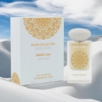 Un flacon de parfum étiqueté "Musk Collection Angel Musk" par Gulf Orchid se trouve à côté de son coffret orné blanc et or assorti, sur un fond blanc lisse et neigeux avec un ciel nuageux. Dakar