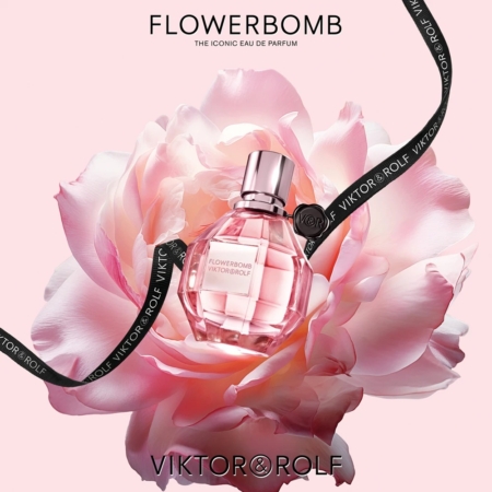 Un flacon rose de Viktor & Rolf Flowerbomb Eau de Parfum pour Femme repose au cœur d'une fleur rose épanouie, rehaussée d'un ruban noir "Viktor & Rolf", le tout sur un fond rose tendre. Dakar