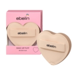 Une houppette de maquillage beige en forme de cœur avec le mot "ebelin" sur sa lanière, présentée à côté de sa boîte d'emballage rose, qui comporte également le logo "ebelin" et des informations sur le produit. Dakar