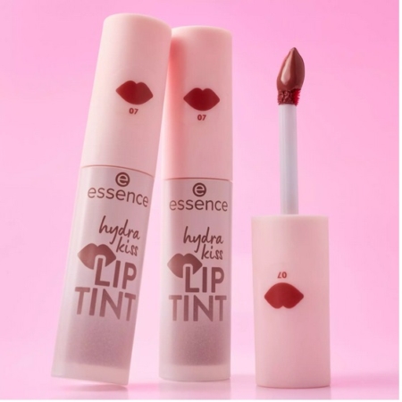 Deux tubes de Essence Hydra Kiss Lip Tint se tiennent debout sur un fond rose, l'un d'eux étant ouvert pour révéler l'applicateur. L'emballage est rose pâle, avec une impression de lèvres et des détails sur le produit en marron. Dakar