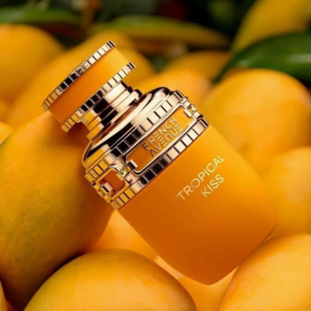 Un flacon de parfum Tropical Kiss de French Avenue en orange vif avec des accents dorés repose sur un lit de mangues mûres, créant une esthétique vibrante et tropicale. Dakar