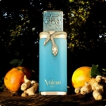 Un flacon de 100 ml de Vulcan Feu Eau de Parfum de French Avenue, de couleur turquoise et orné d'un serpent doré, est exposé parmi des racines de gingembre et des grenades, avec la lumière du soleil et des arbres feuillus en arrière-plan. Dakar