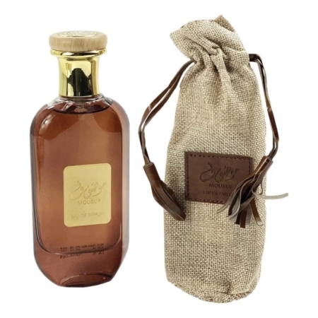 Un flacon de parfum en verre brun avec un bouchon et une étiquette dorés se trouve à côté d'une pochette à cordon en toile de jute beige assortie avec une étiquette en cuir brun. Dakar