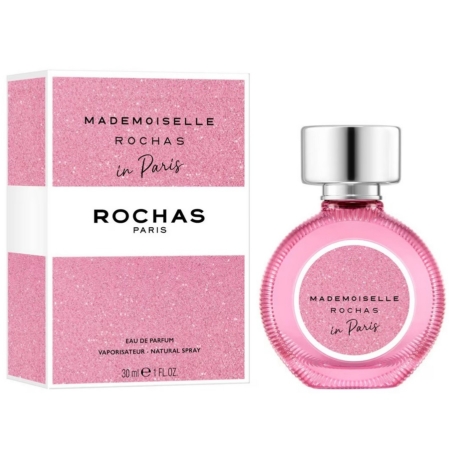 Une boîte rose et un flacon de parfum rose rond assorti, étiqueté "Mademoiselle Rochas in Paris" par Rochas Paris, présentés côte à côte. Le flacon est muni d'un bouchon argenté et d'une étiquette rose pailletée. Dakar