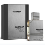 Une boîte métallique argentée et noire étiquetée "Al Haramain Amber Oud Carbon Edition Eau de Parfum 100 ml" se trouve à côté d'un flacon de parfum rectangulaire assorti avec un bouchon argenté et le même marquage. Dakar