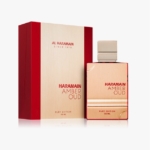 Un flacon de parfum or et rouge étiqueté "Haramain Amber Oud Ruby Edition 120 ML" se trouve à côté d'une boîte or et rouge assortie, avec un texte et une marque similaires. Dakar