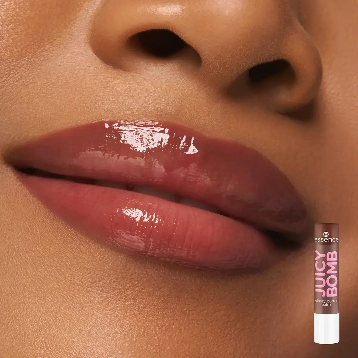 Gros plan sur les lèvres brillantes et bien hydratées d'une personne, avec une teinte rose naturelle. Dans le coin inférieur droit, le produit utilisé est un tube de baume à lèvres Essence Juicy Bomb. Dakar