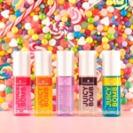 Cinq tubes de gloss Essence Juicy Bomb de différentes couleurs sont présentés en rangée, sur fond de bonbons colorés et vibrants, avec des sucettes, des bonbons à la gomme et des sucreries. Dakar