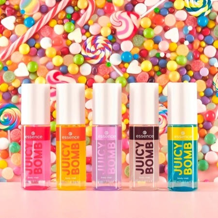 Cinq tubes de gloss Essence Juicy Bomb de différentes couleurs sont présentés en rangée, sur fond de bonbons colorés et vibrants, avec des sucettes, des bonbons à la gomme et des sucreries. Dakar