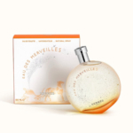 Le flacon rond et orangé du parfum Hermès Eau des Merveilles est présenté devant son coffret blanc et orange assorti, illustré d'une calèche. Dakar
