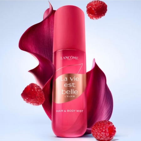 Un flacon rose de Lancôme La Vie Est Belle L'Elixir Hair & Body Mist est entouré de pétales roses et de framboises flottantes sur un fond bleu clair. Dakar