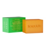 Deux barres orange de Makari Kojic Acid Dark Spot Remover Exfoliating Soap sont présentées à côté d'un emballage vert qui met en évidence ses ingrédients : vitamine C, rétinol et collagène. Le mot "Makari" figure sur les barres de savon. Dakar