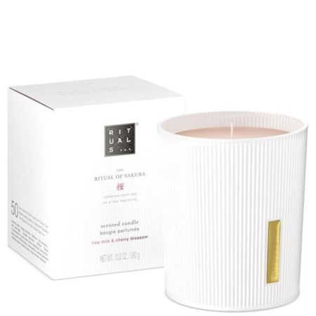 Une bougie parfumée Rituals The Ritual of Sakura blanche dans un récipient en verre strié est posée à côté de sa boîte blanche assortie, étiquetée avec un parfum de lait de riz et de fleurs de cerisier. Dakar
