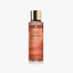 Une bouteille de brume de parfum Victoria's Secret Amber Romance avec une étiquette orange, un bouchon doré et un corps transparent, montrant le liquide ambré à l'intérieur. Le texte sur le flacon indique la marque et le nom du produit. Dakar