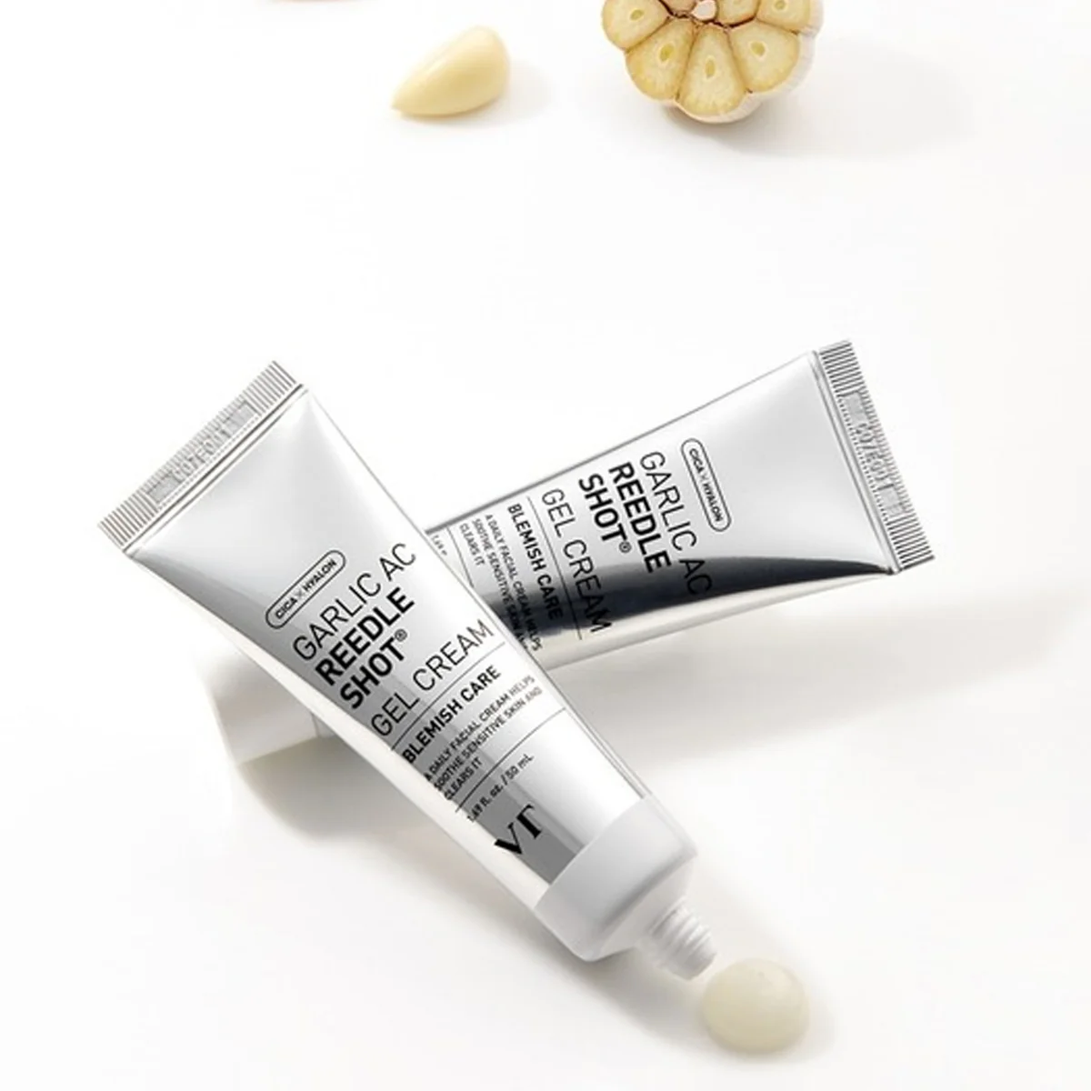 Deux tubes de VT Cosmetics Crème Gel à l'Ail Apaisante et Unifiante AC Reedle Shot 50ml reposent sur une surface blanche, avec un peu de crème visible à proximité et de l'ail en arrière-plan. Dakar