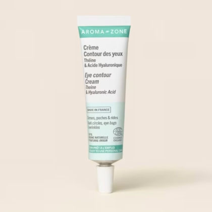Un tube d'Aroma Zone Crème Contour des Yeux Cernes Poches et Rides 15ml se tient debout sur un fond beige clair, avec des étiquettes en français et en anglais, et formulé avec de la théine et de l'acide hyaluronique. Dakar