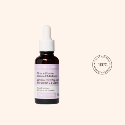 Un flacon compte-gouttes en verre brun étiqueté "Aroma Zone Anti Taches Oléosérum Vitamine C et Glabridine Peau Terne 30ml" est posé sur un fond beige clair, à côté d'un tampon rond indiquant "100% Pure et Naturelle". Dakar