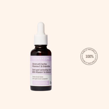 Un flacon compte-gouttes en verre brun étiqueté "Aroma Zone Anti Taches Oléosérum Vitamine C et Glabridine Peau Terne 30ml" est posé sur un fond beige clair, à côté d'un tampon rond indiquant "100% Pure et Naturelle". Dakar