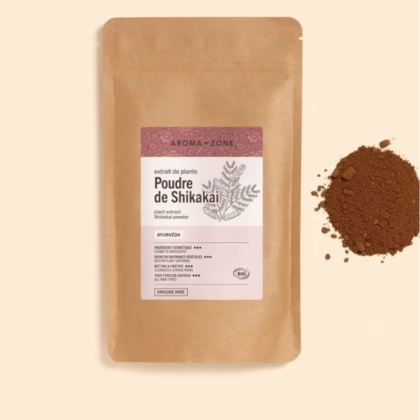 Un sachet en papier marron étiqueté "Aroma Zone Shikakai en Poudre Bio Anti Chute 250g" avec un dessin botanique repose à côté d'un petit monticule de poudre brun-rouge sur un fond beige. Dakar