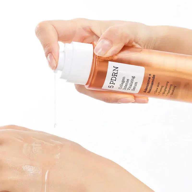 Une main pompe du sérum transparent d'un flacon étiqueté "5 PDRN" sur le dos d'une autre main, sur un fond blanc. Dakar