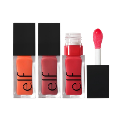 Trois Elf Huile à Lèvres Revitalisante Glow Reviver de 7,6 ml dans les teintes orange, mauve et rouge sont présentés, l'un d'entre eux étant ouvert pour révéler un applicateur teinté de rose. Les tubes transparents ont un couvercle noir. Dakar
