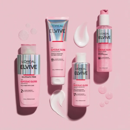 Quatre produits de soins capillaires L'Oréal Elvive Glycolic Gloss, de couleur rose, comprenant un shampooing, un après-shampooing, un gloss et un sérum, sont disposés sur un fond rose, avec des échantillons de produits et des gouttes à proximité. Ils sont disponibles chez Univers Cosmetix. Dakar