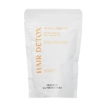 Un sachet blanc étiqueté "HAIR DÉTOX RESOLUTION N°2" avec un texte orange et noir, décrit comme un thé capillaire biologique aux propriétés anti-chute, purifiantes et hydratantes. Marque : Madame La Présidente. Dakar