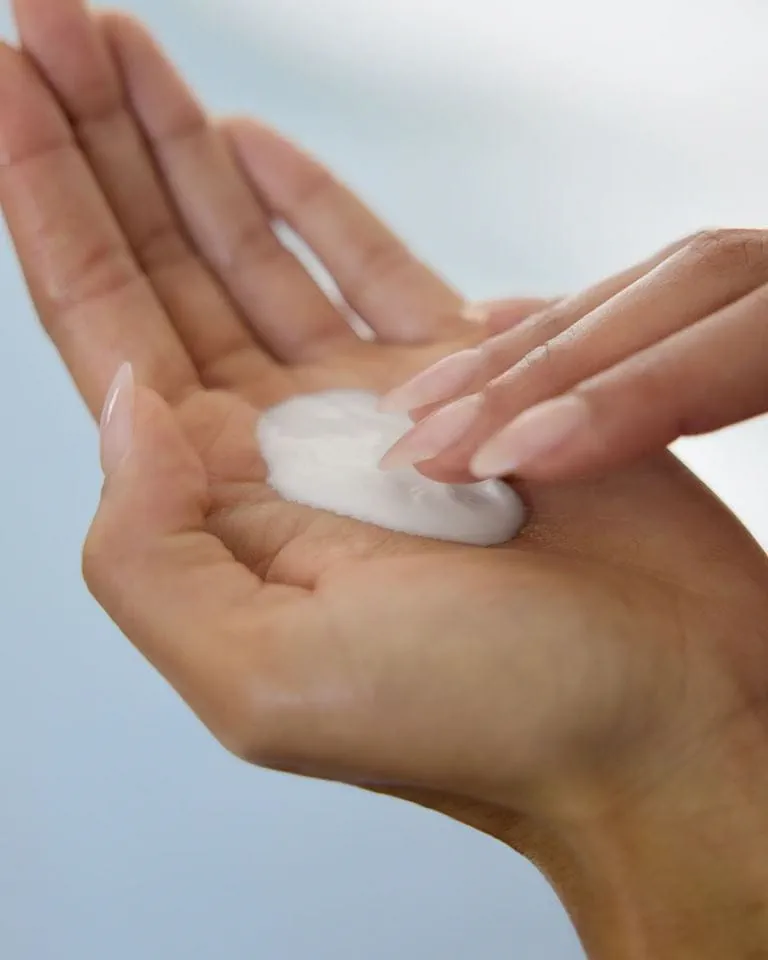 Un gros plan montre une personne tenant Nivea Crème de Douche Exfoliante pour Corps 200 ml dans une main tout en ramassant ou en étalant délicatement la crème avec deux doigts, sur un fond légèrement flou. Dakar