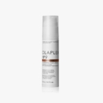 Un flacon blanc de Olaplex N°9 Bond Protector Sérum Nourrissant Pour Cheveux 90ml avec un bouchon transparent se tient debout sur un fond blanc uni. L'étiquette comporte un texte noir et cuivre. Dakar