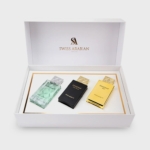 Un coffret cadeau blanc portant la marque "Swiss Arabian", contenant trois flacons de parfum - un vert transparent, un noir et un doré - soigneusement disposés à l'intérieur avec des accents dorés. Dakar