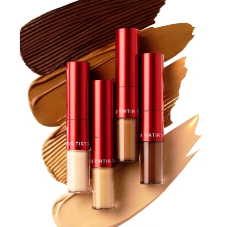Quatre tubes de Correcteur Floutant Double Action Glide an Hide avec des bouchons rouges métalliques sont disposés verticalement au-dessus d'échantillons de fond de teint dans différentes teintes de beige clair à foncé et de brun, sur un fond blanc. Dakar