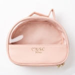 La Trousse Musc Intime est une trousse à cosmétiques rose avec une face avant transparente, des fermetures éclair dorées, une petite poignée supérieure et la mention "MUSC intime" en lettres dorées sur la face avant. Dakar