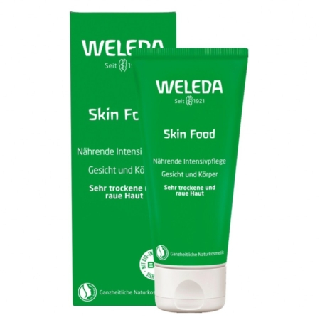 Un tube vert de la crème hydratante Weleda Skin Food se trouve devant sa boîte verte assortie. Tous deux affichent un texte blanc en allemand et en anglais, indiquant que le produit est destiné aux peaux très sèches et rugueuses du visage et du corps. Dakar