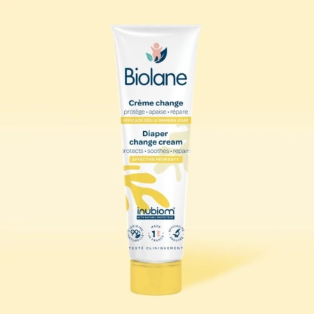 Un tube de Biolane Crème change Bébé 100ml se tient debout sur une surface jaune clair avec un fond assorti. L'emballage comporte des textes et des graphiques blancs, bleus et jaunes présentant les avantages du produit en français et en anglais. Dakar