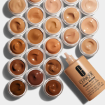 Des rangées de contenants de maquillage ouverts présentent une gamme de teintes de fond de teint allant du clair au foncé. Sur le côté droit, on trouve un flacon de Clinique Even Better Fond de Teint Spf15 Éclat Correction Teint 30ml. Dakar