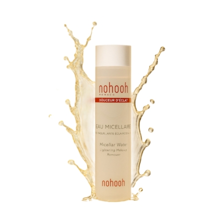 Un flacon de 200 ml de Nohooh Eau Micellaire Démaquillant Éclaircissant se tient debout avec une éclaboussure de liquide derrière lui sur un fond blanc. L'étiquette indique "Démaquillant Éclaircissant" avec des accents rouges et blancs. Dakar