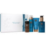Un coffret cadeau Rituals comprenant quatre produits de soins bleus et bruns devant une boîte blanche aux accents bleus. On peut y lire : "Le bonheur peut se trouver dans les plus petites choses. Dakar