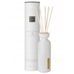 Un flacon diffuseur en céramique blanche avec plusieurs bâtonnets de roseau à côté d'une grande boîte cylindrique étiquetée "Rituals... The Ritual of Sakura" et "blossoming blossoms fragrance oil, rice milk & cherry blossom. Dakar