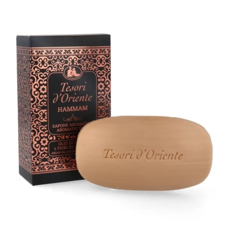 Un pain de savon portant l'inscription "Tesori d'Oriente" est posé devant une boîte décorative noire et cuivre assortie, étiquetée "Tesori d'Oriente Hammam Sapone Aromatico" avec de l'huile d'argan et de la fleur d'oranger. Dakar