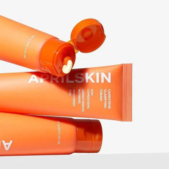 On voit trois tubes orange de la Crème Clarifiante et Équilibrante pour Peaux à Imperfections d'AprilSkin (60 ml) posés sur un fond blanc ; l'un d'entre eux est ouvert, laissant apparaître la crème, tandis que toutes les informations sur le produit et le logo de la marque sont bien visibles. Dakar