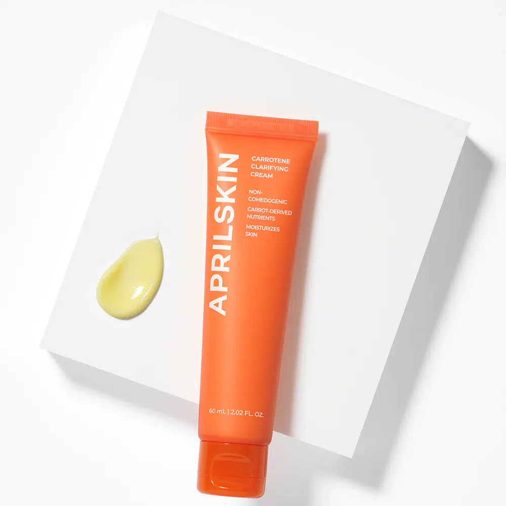Un tube orange de la Crème Clarifiante et Équilibrante pour Peaux à Imperfections d'AprilSkin (60 ml) repose sur une surface blanche, à côté d'une petite flaque de crème jaune pâle, mettant en avant ses bienfaits clarifiants et équilibrants pour les peaux sujettes aux imperfections. Dakar