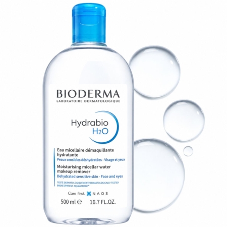 On voit un flacon transparent d'eau micellaire Bioderma Hydrabio H2O, muni d'un bouchon bleu, présenté à la verticale, à côté de trois gouttelettes d'eau sur un fond blanc. L'étiquette met en avant ses propriétés hydratantes et démaquillantes. Dakar