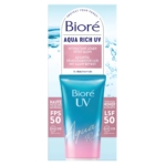 Une boîte de Bioré Fluide Solaire Hydratant SPF 50 Aqua Riche UV Effet Glow de 50 ml se présente sous la forme d'un tube bleu et rose, portant la mention « Hydratant Léger Effet Glow », la mention « haute protection quotidienne » et un fond inspiré de l'eau. Dakar