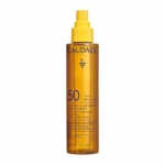 Un flacon vaporisateur jaune de 150 ml de « Vinosun SPF 50 Huile Solaire Sublimatrice Très Haute Protection Visage, Corps et Cheveux » de Caudalie, muni d’un bouchon jaune et d’une inscription en violet foncé, portant la mention « Huile Sublimatrice Haute Protection » pour le visage, le corps et les cheveux. Dakar