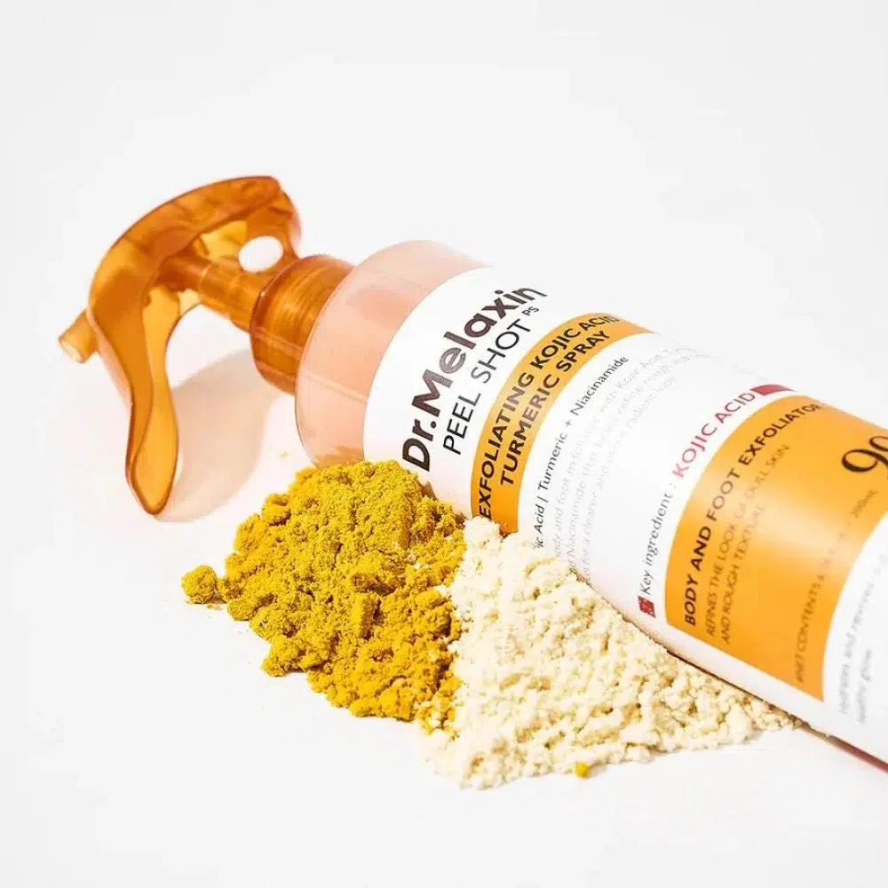 Un flacon Dr Melaxin Spray Exfoliant à l'Acide Kojique et au Curcuma Peel Shot de 200 ml est représenté couché sur le côté à côté de petits tas de poudres jaunes et beiges sur un fond blanc. Dakar