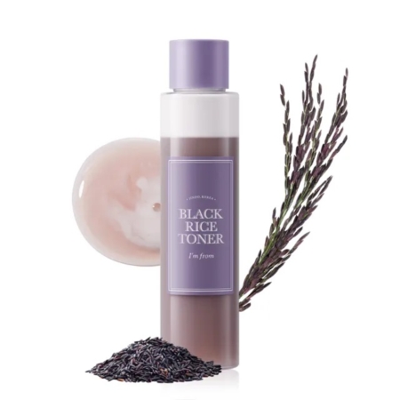 Un flacon de "I'm From Lotion Tonique au Riz Adoucissante et Hydratante 150 ml (Copie)" avec un bouchon et une étiquette en lavande est représenté à côté de riz noir, d'une brindille de lavande et d'un échantillon sur un fond blanc. Dakar