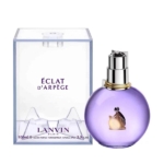 Un flacon de parfum rond, de couleur lavande, muni d'un vaporisateur argenté, repose à côté d'un coffret rectangulaire transparent portant l'inscription « Éclat d'Arpège » de Lanvin Paris. Le flacon est orné d'un logo en silhouette dorée. Dakar